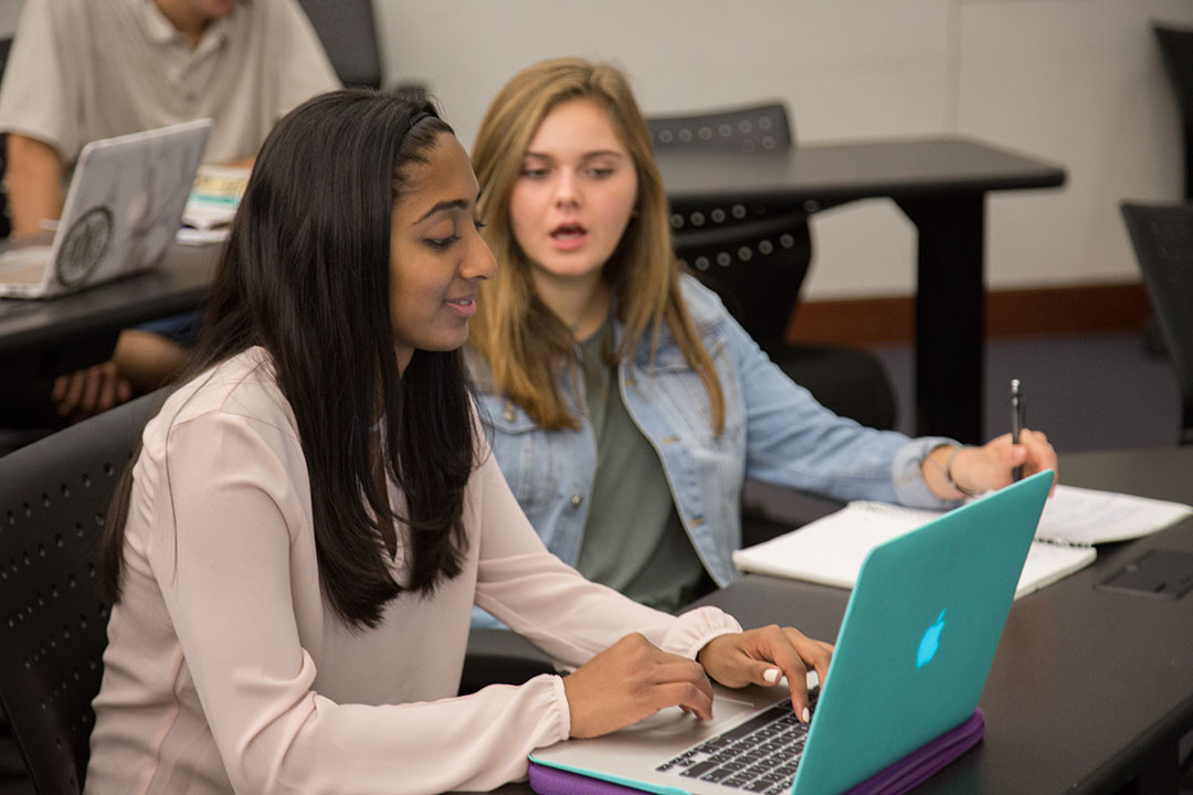 Two students talking behind a laptop